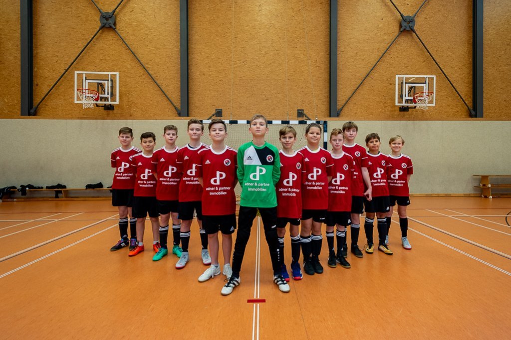 Jugendarbeit in Braunschweig – Sportförderung durch Adner & Partner Immobilien Jugendfußballmannschaft in roten Trikots mit Trainern bei einem Hallenturnier als Beispiel für die regionale Sportförderung von Adner & Partner Immobilien